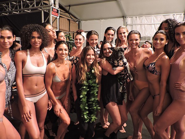 The Acacia Swimwear Post-Runway Show Pic;  Lyndie Irons, Acacia's co-owner, is wearing a green lei in the middle. Naomi Newirth, Acacia's designer and co-owner,  is holding a dog. Models from the label's July 19 runway show wear Acacia Swimwear.